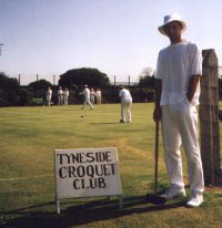 Photo of John Moore in croquet whites and floppy sunhat standing beside a Tyneside Croquet Club sign.